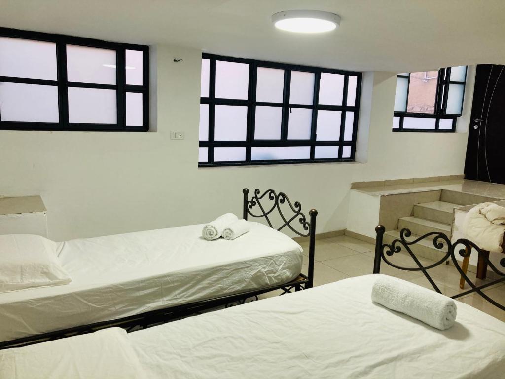 two beds in a room with windows at צימר בצפת, מרווח ושקט, חצר גדולה, מיועד לשומרי שבת, ישנן שתי מיטות רגילות ועוד שתיים מתקפלות, ארבע מיטות סך הכל in Safed