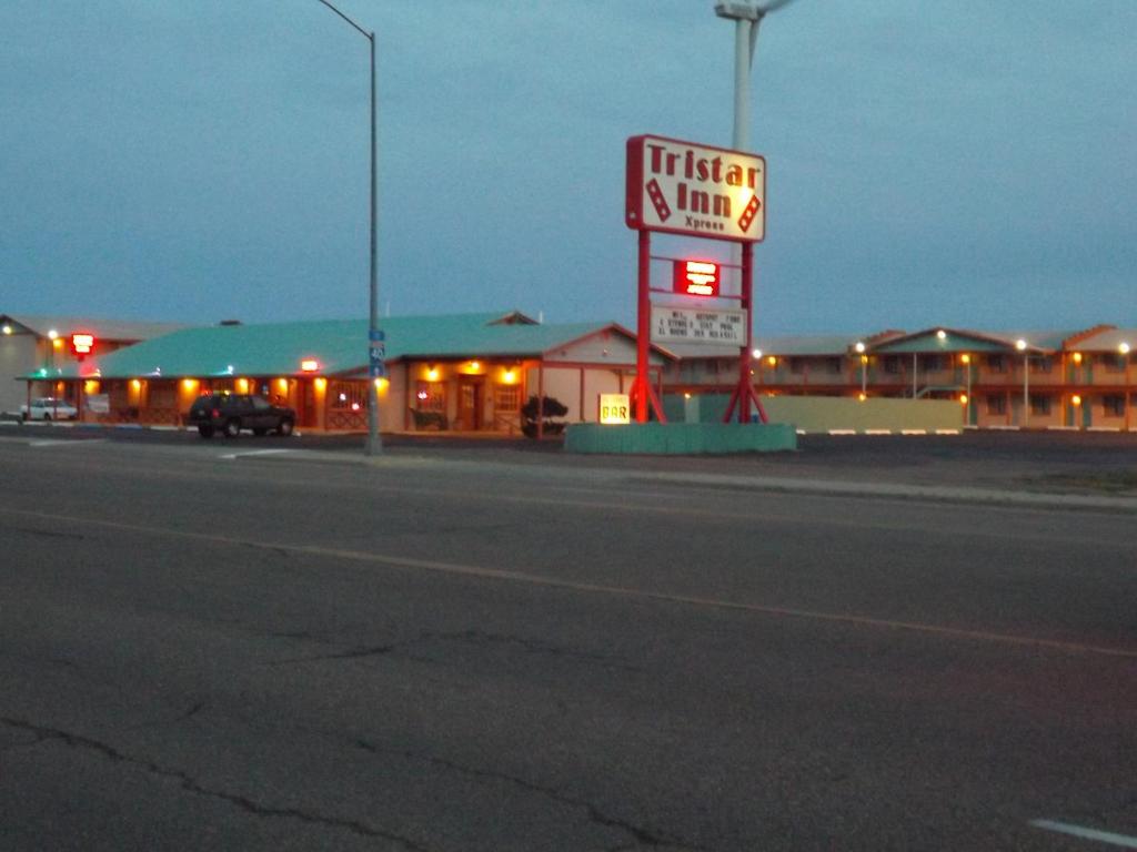 un cartello di fronte a un distributore di benzina di notte di Tristar Inn Xpress a Tucumcari