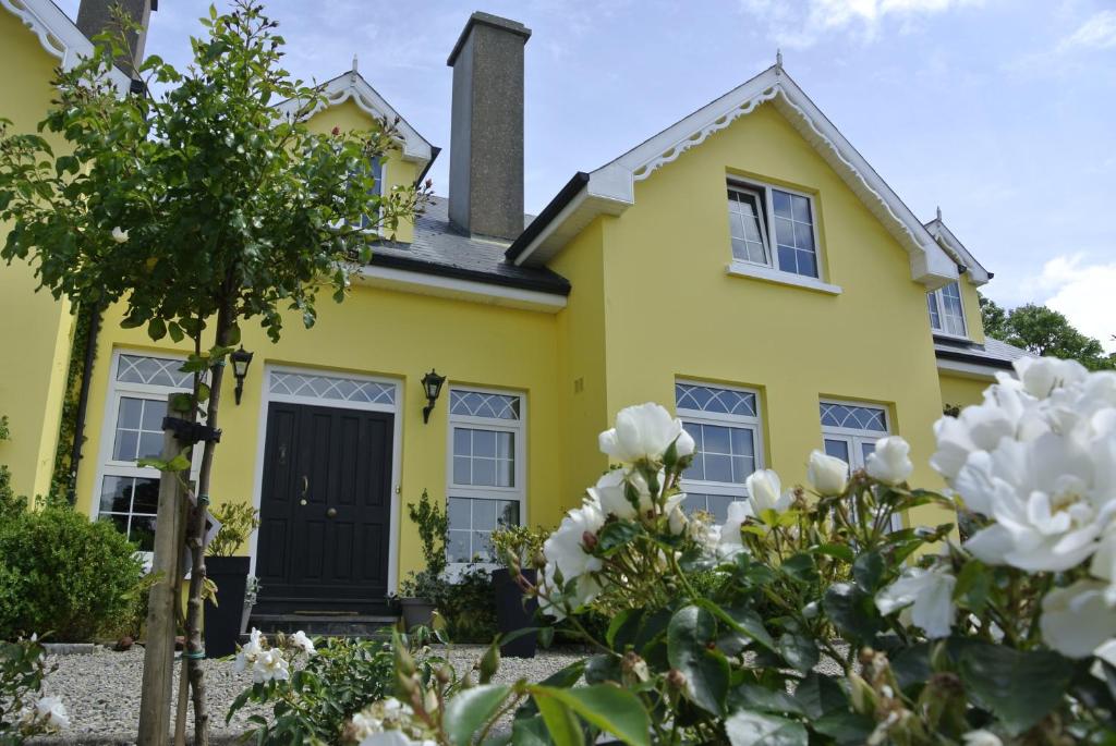 Drumcreehy Country House B&B في باليفاوغان: منزل أصفر مع زهور بيضاء في الأمام