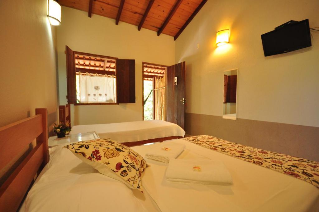 a bedroom with two beds and a flat screen tv at TEMPLÁRIOS ECOVILLA Pousada in Pirenópolis