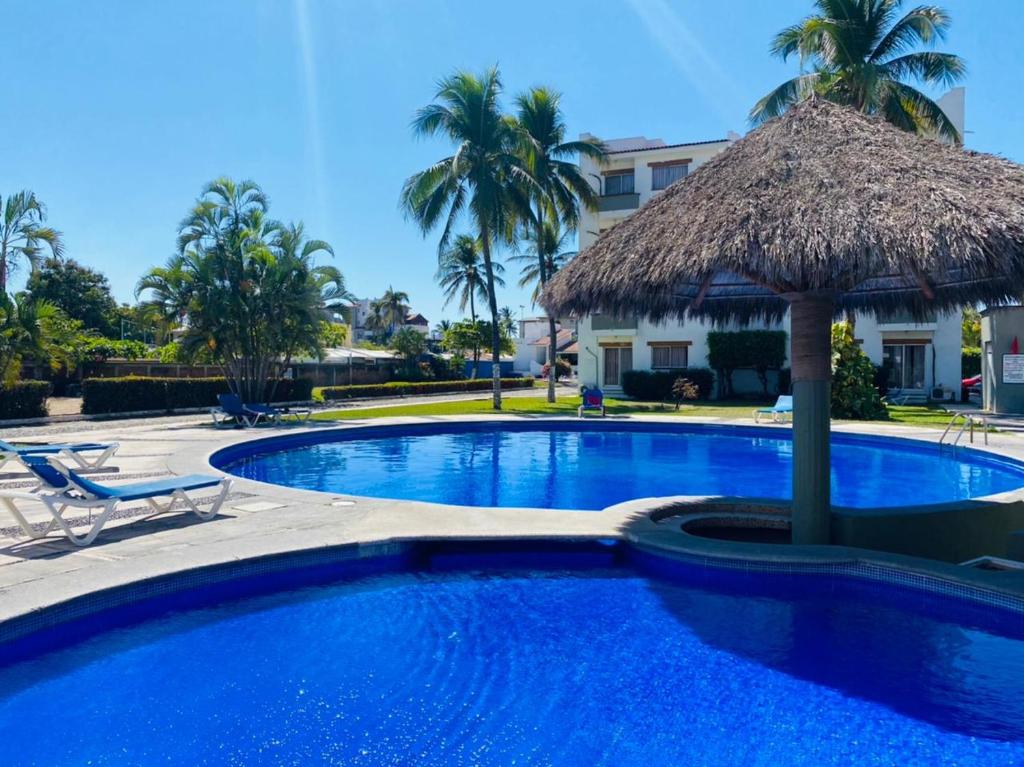 ein Pool mit einem Strohschirm und Palmen in der Unterkunft Cocotero Manzanillo in Manzanillo