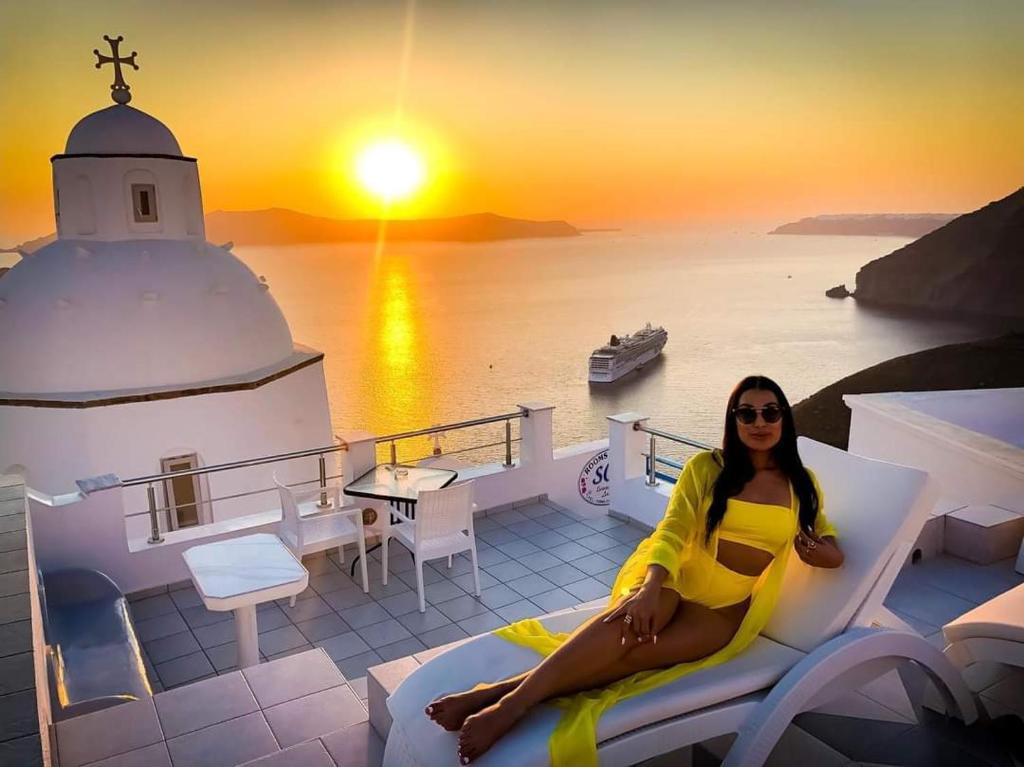 a woman sitting on a bench on a balcony with a sunset at Sofi Rooms in Fira