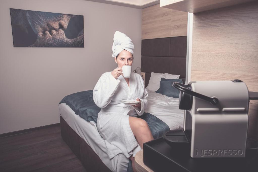 a woman sitting on a bed drinking a cup of coffee at Klima Hotel Europarc in Kerpen