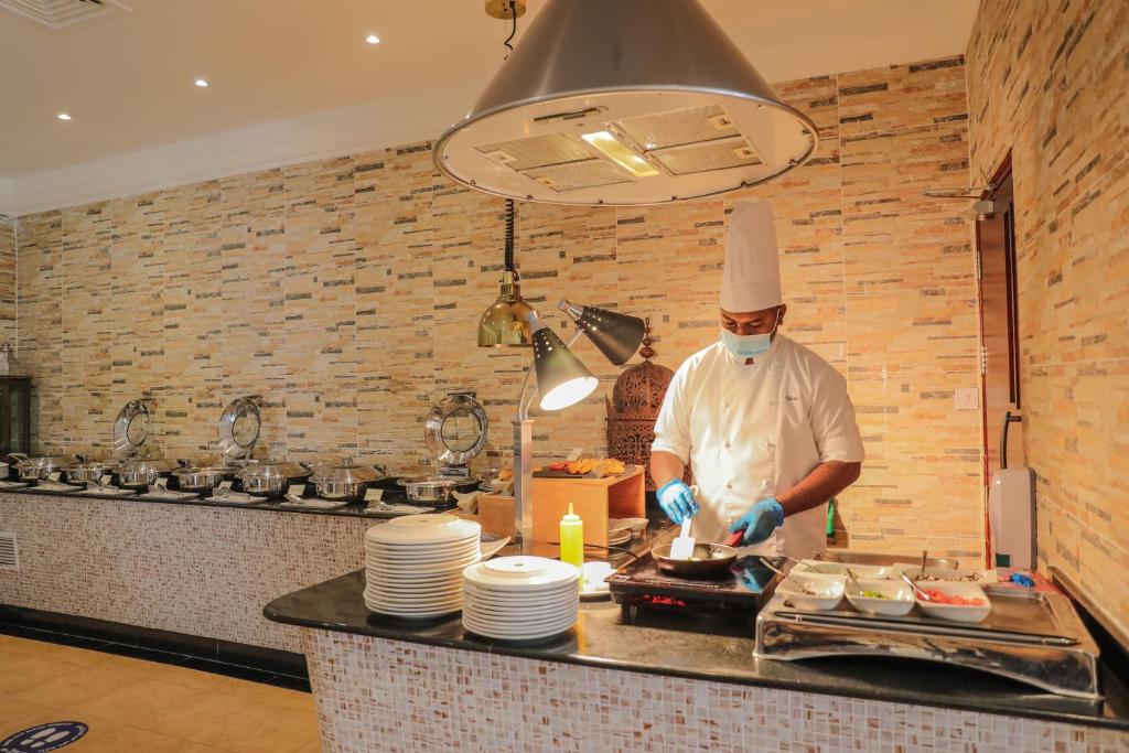 a chef standing in a kitchen preparing food at Dhafra Beach Hotel in Jebel Dhanna