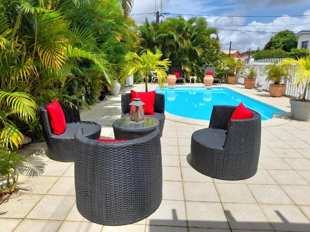 a group of wicker chairs with red pillows next to a pool at COQUET F2 CLIMATISE AVEC PISCINE AU LAMENTIN in Le Lamentin