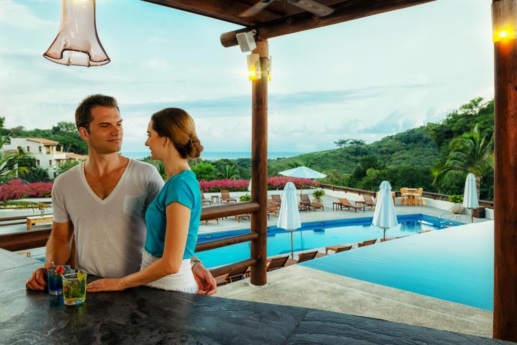 Couple at swim-up bar overlooking pool and tropical hillside landscape.
