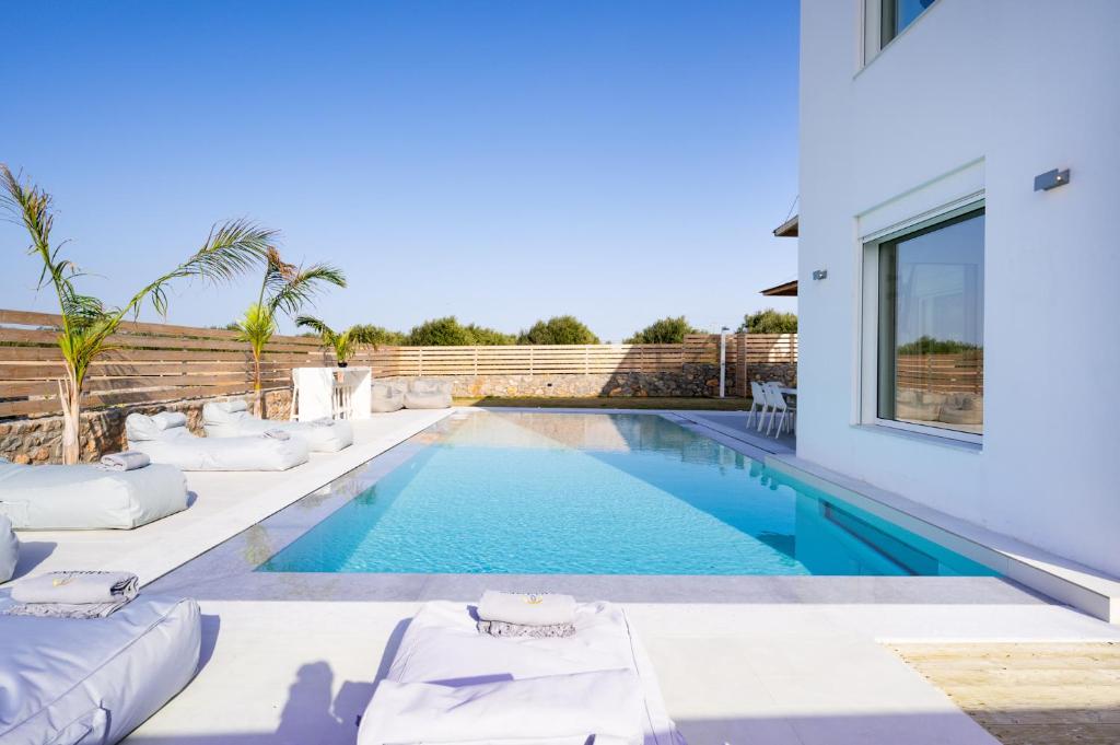 a swimming pool with white furniture next to a house at Sardines Luxury Villas in Analipsi