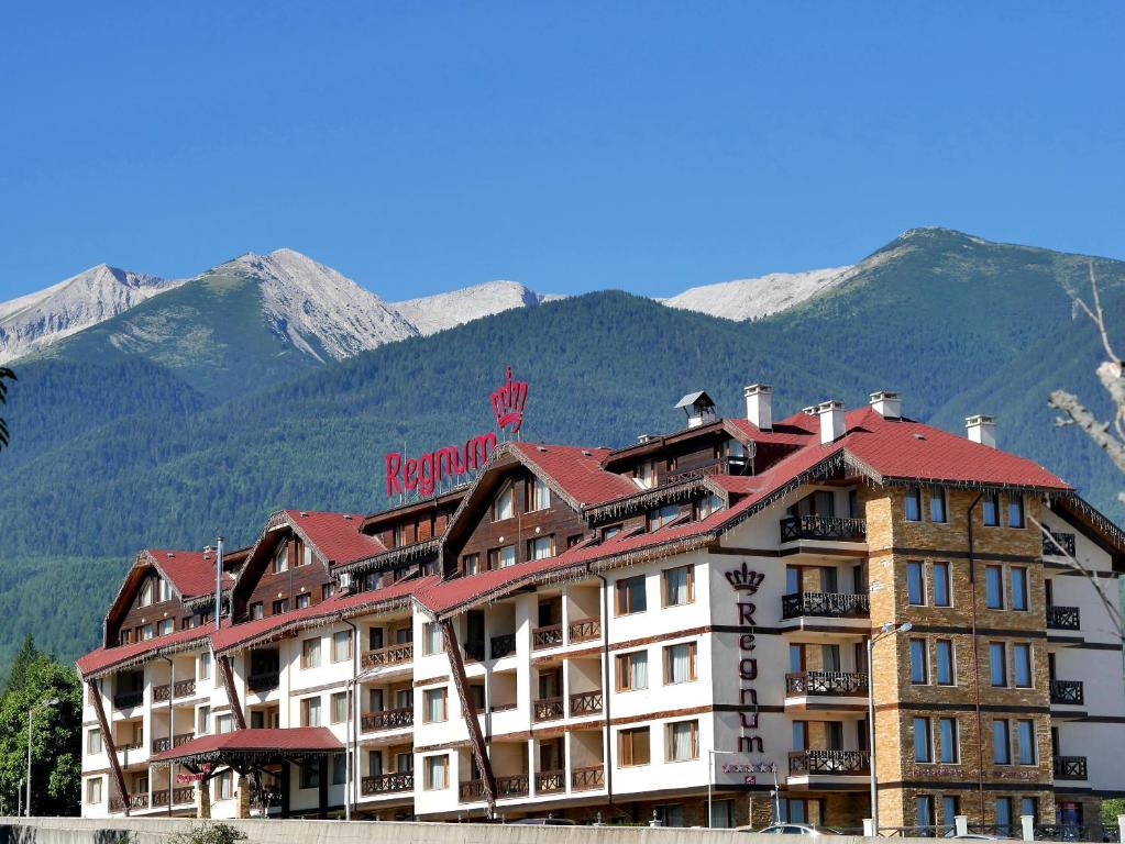 un bâtiment d'hôtel avec des montagnes en arrière-plan dans l'établissement Regnum Bansko Ski Hotel & SPA, à Bansko