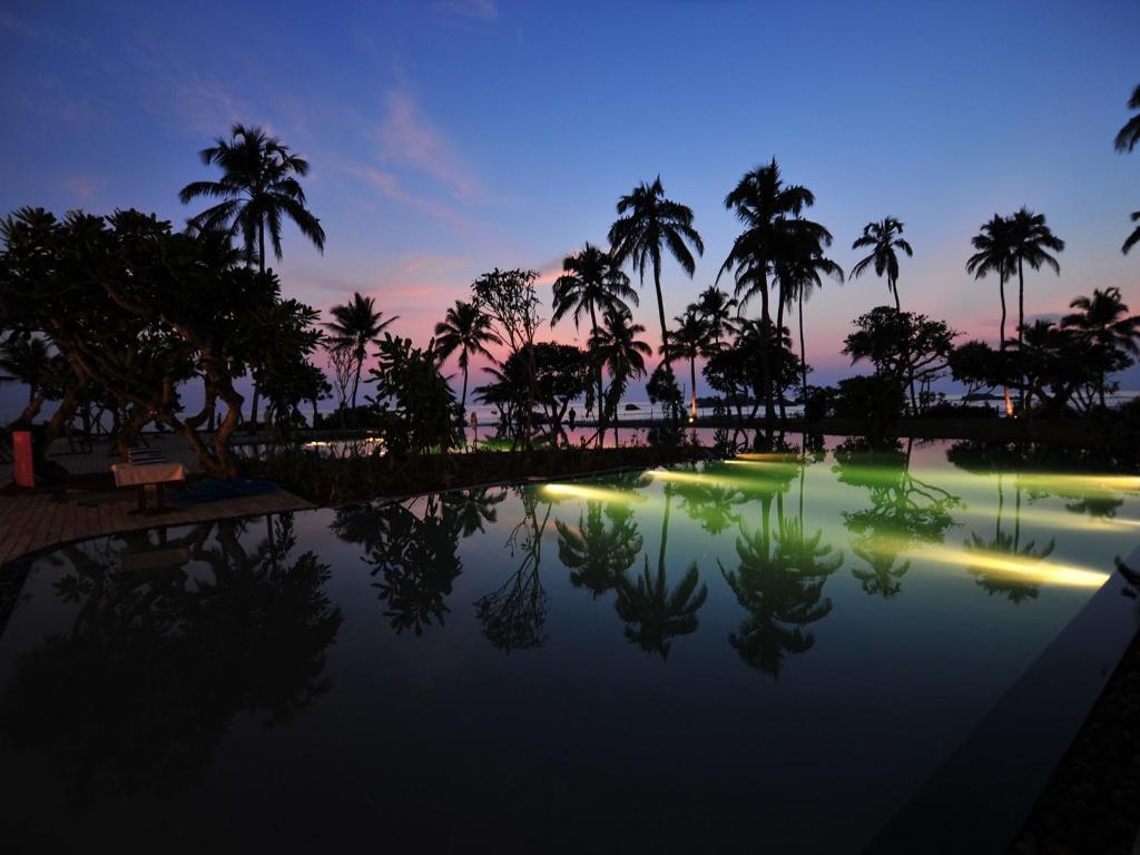 a pool of water with palm trees at night at Hikka Tranz by Cinnamon in Hikkaduwa