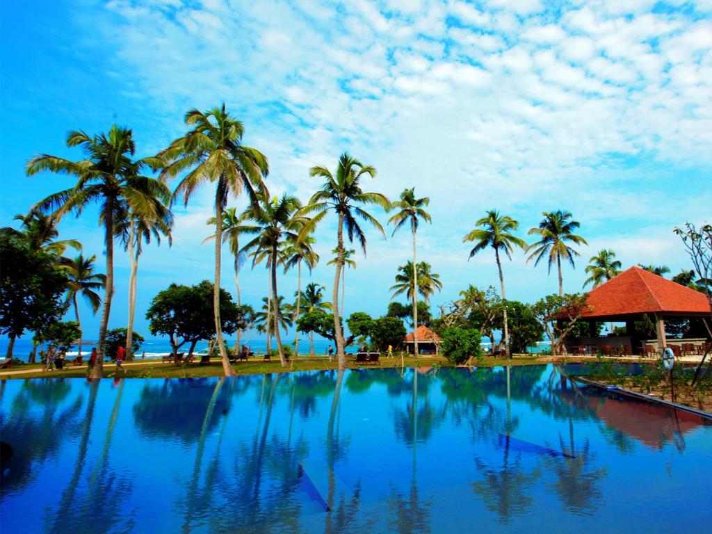a pool with palm trees and a blue sky at Hikka Tranz by Cinnamon in Hikkaduwa