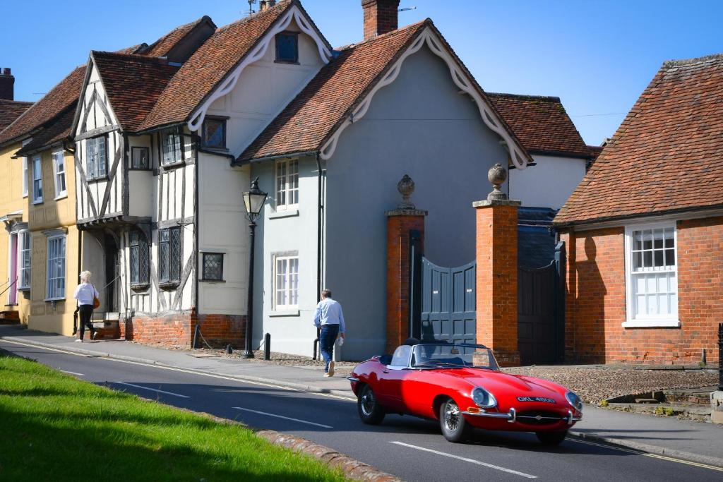 een rode auto rijdt door een straat met huizen bij The Gate Cottage in Thaxted