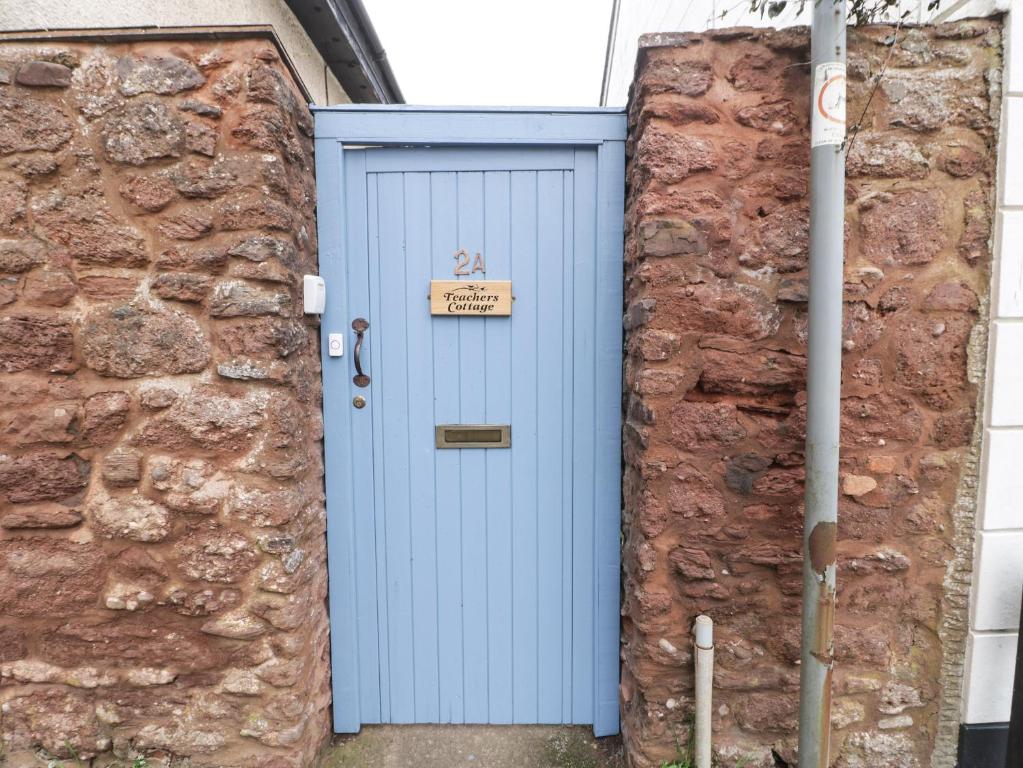 uma porta azul numa parede de tijolos com um sinal em Teacher's Cottage em Taunton