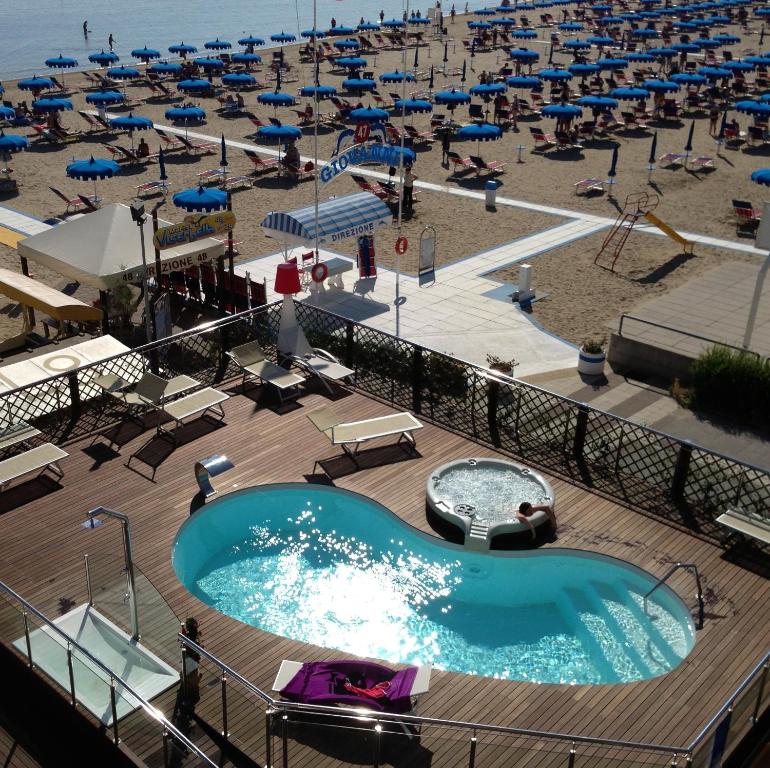 una piscina e una spiaggia con sedie e ombrelloni di Hotel Baia a Rimini