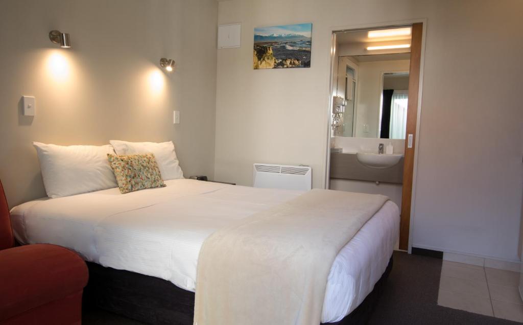 Bella Vista Motel Kaikoura في كايكورا: غرفة نوم بسرير ابيض كبير وحمام