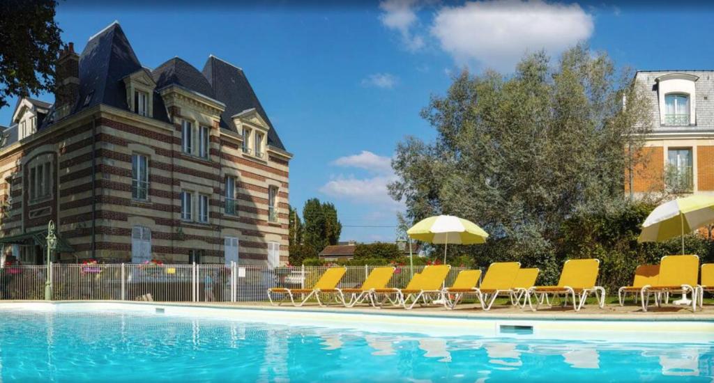 - une piscine avec des chaises et des parasols à côté d'un bâtiment dans l'établissement Cosy appartement dans une villa avec piscine, proche du centre et de la mer, à Cabourg