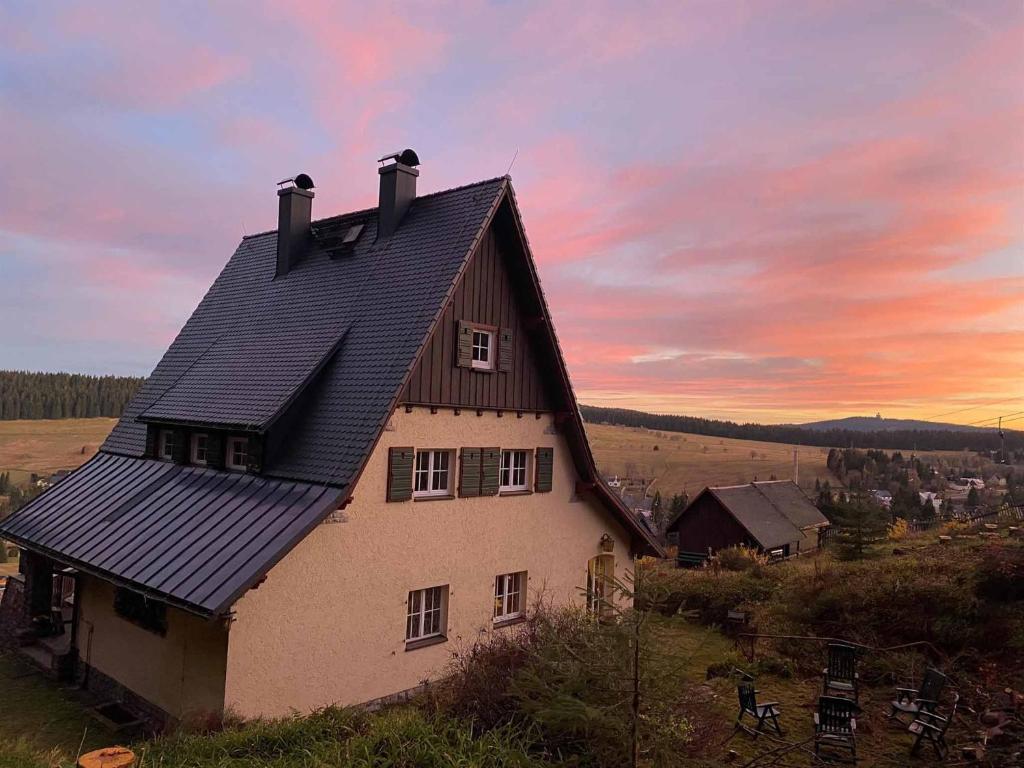 een huis met een zwart dak met een zonsondergang op de achtergrond bij Berghaus Carlsfeld in Eibenstock