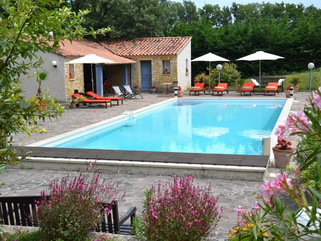 una piscina en un patio con sillas y sombrillas en La Devinière en Donzère