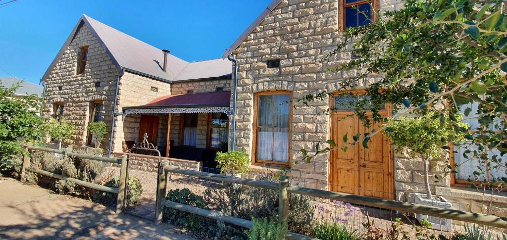 a stone house with a wooden door and a fence at Oudeklip Guesthouse Nieuwoudtville in Nieuwoudtville