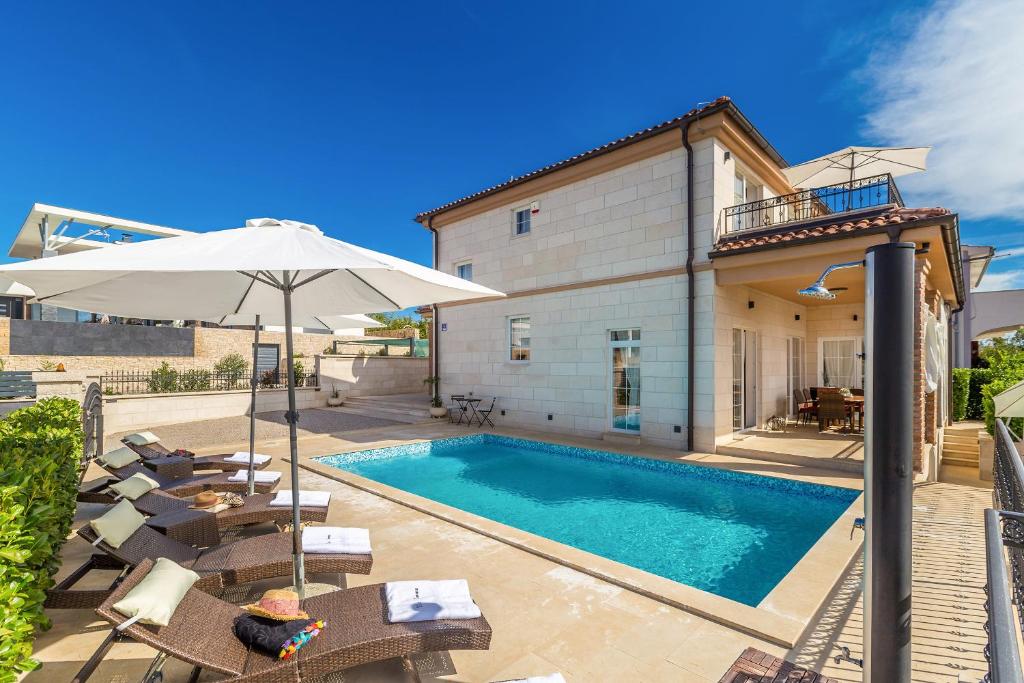 a swimming pool with chairs and an umbrella next to a house at Villa Emma - Linardići - Krk in Linardići