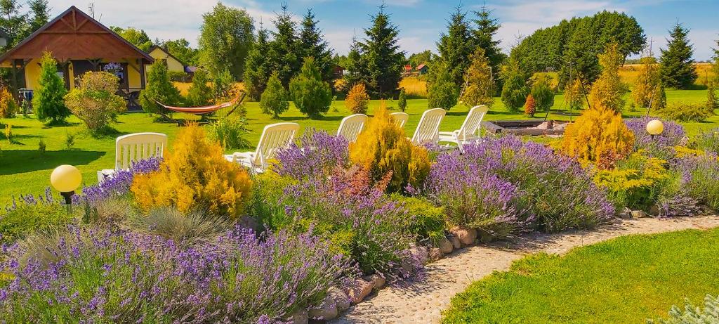 un jardín con sillas blancas y flores púrpuras en Domki Przyjazna Osada en Darłowo