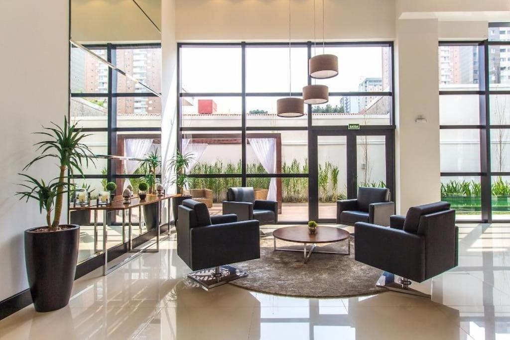 a lobby with chairs and a table and large windows at 709- Apartamento Decorado Encantador, mobiliado, amplo, cozinha completa, Excelente localização no Rebouças in Curitiba