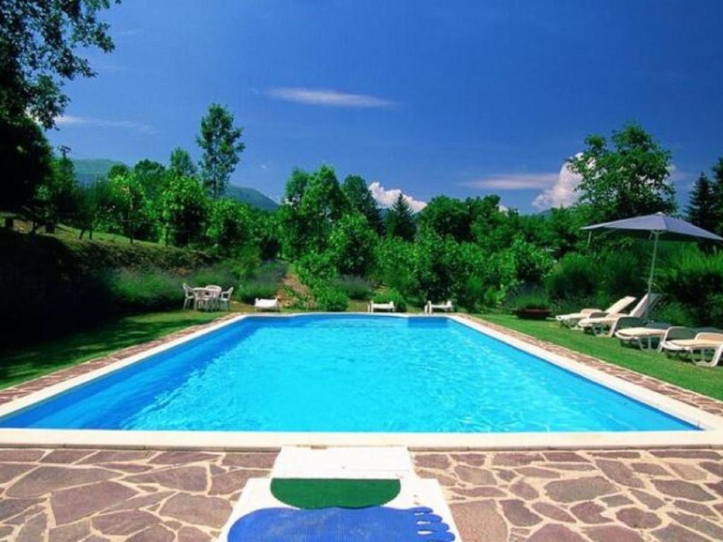 a large swimming pool with chairs and an umbrella at Belvilla by OYO Fattoria 15 in Amandola