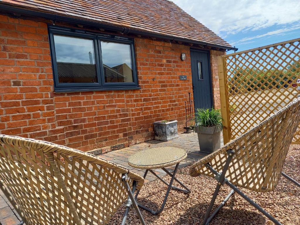 a patio with a chair and a table in front of a brick building at The Cow Shed, Kenilworth, Sleeps 2 in Kenilworth