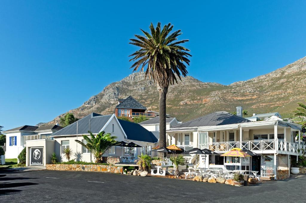 a house with a palm tree in front of a mountain at Boulders Beach Hotel, Cafe and Curio shop in Simonʼs Town