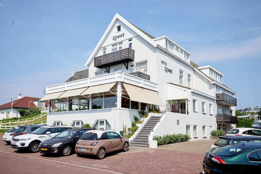 ein weißes Gebäude mit Autos auf einem Parkplatz in der Unterkunft Hotel Zonne in Noordwijk aan Zee