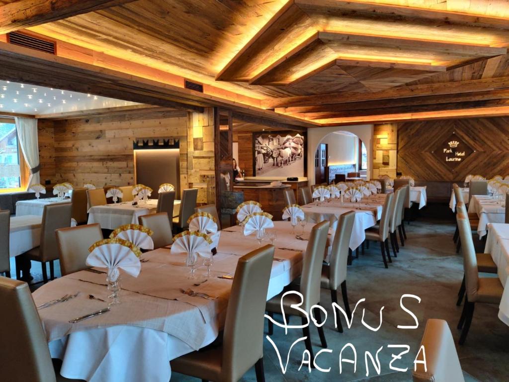 a dining room with white tables and chairs and wooden ceilings at Hotel Laurino in Pozza di Fassa