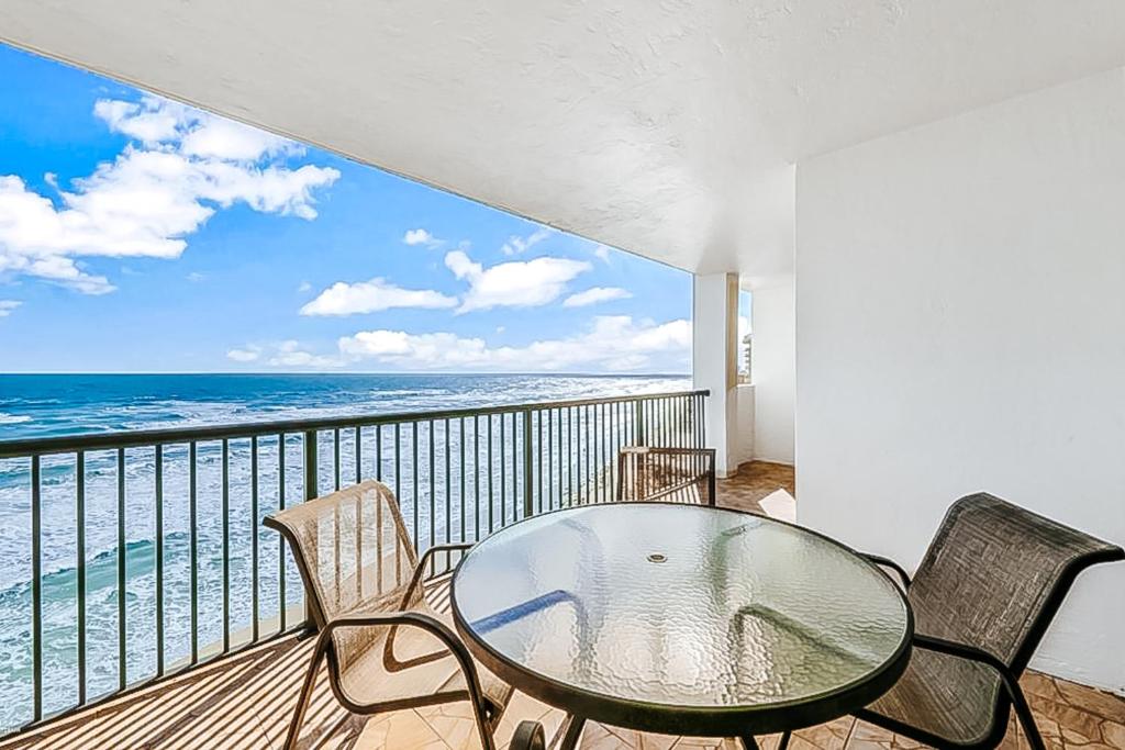 a balcony with a glass table and chairs and the ocean at Daytona Beach Soaring in Daytona Beach Shores