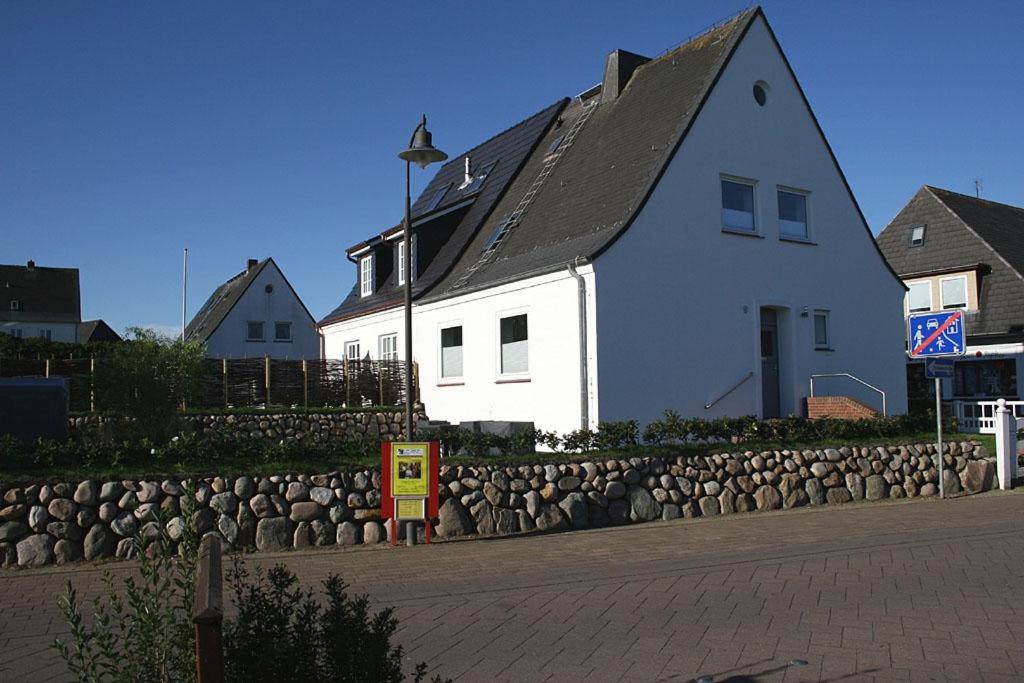 ein weißes Haus mit einer Steinmauer neben einem Gebäude in der Unterkunft Ferienhaus TerpMeren in Hörnum