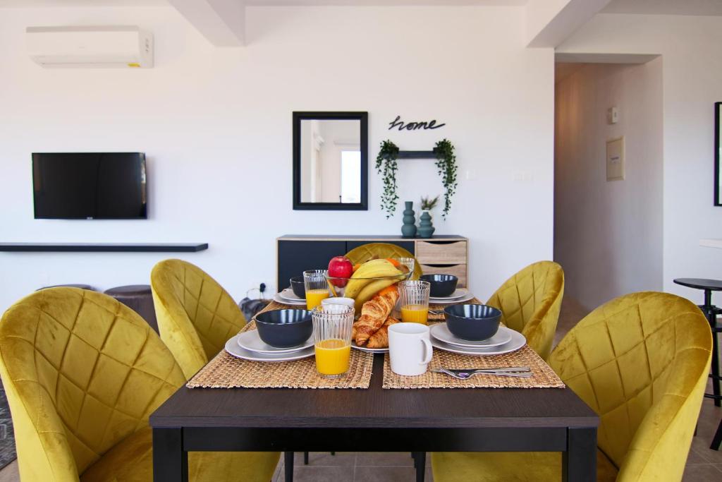 a dining room table with yellow chairs and a table with food at Phaedrus Living Cityview Luxury Flat Walnut Grove in Paphos