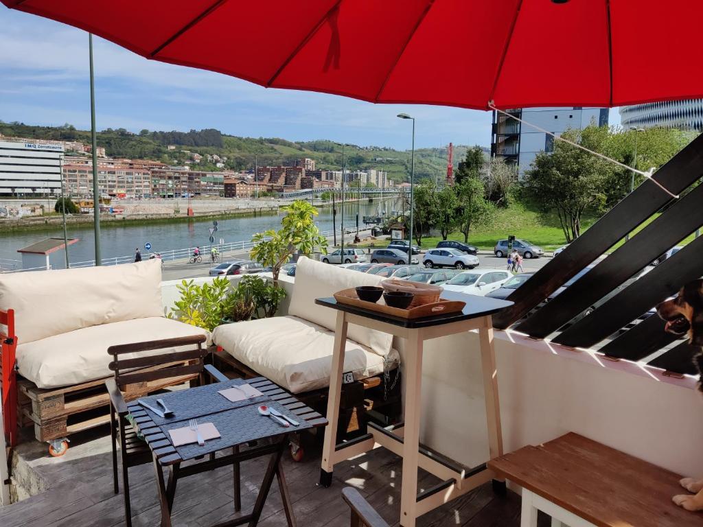 einen Balkon mit einem roten Regenschirm, einem Tisch und Stühlen in der Unterkunft Amets house in Bilbao