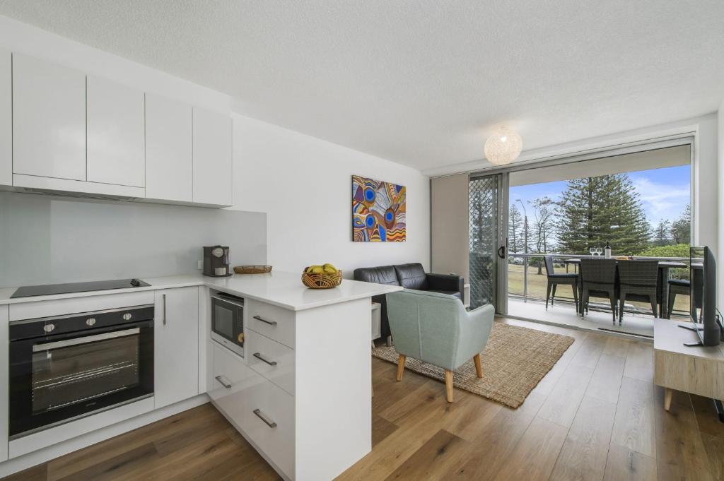 a kitchen with white cabinets and a living room with a table at Ocean Court 5 13 Lord Street in Port Macquarie