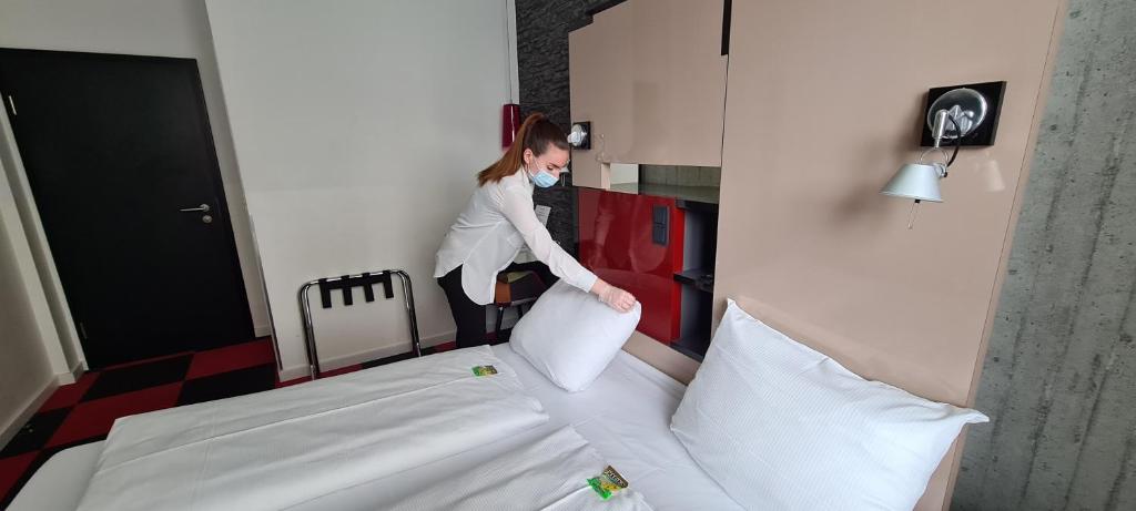 a woman is making a bed in a room at Hotel Cristall - Frankfurt City in Frankfurt/Main