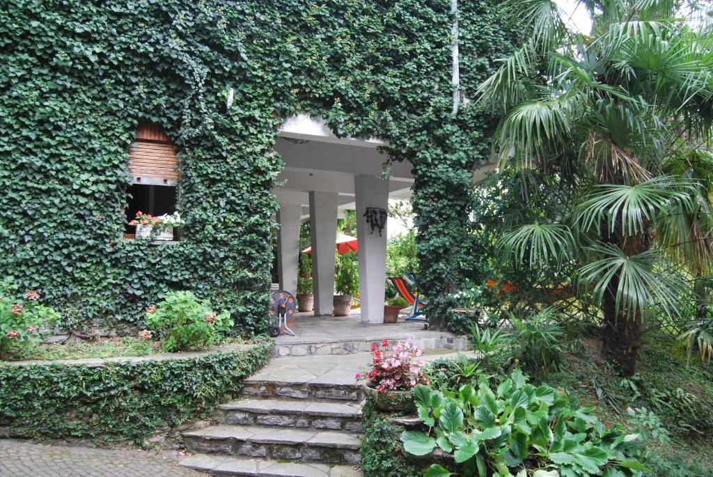 a building covered in green ivy with a pathway and flowers at B&B Le Ortensie -Lago di Como in Lierna