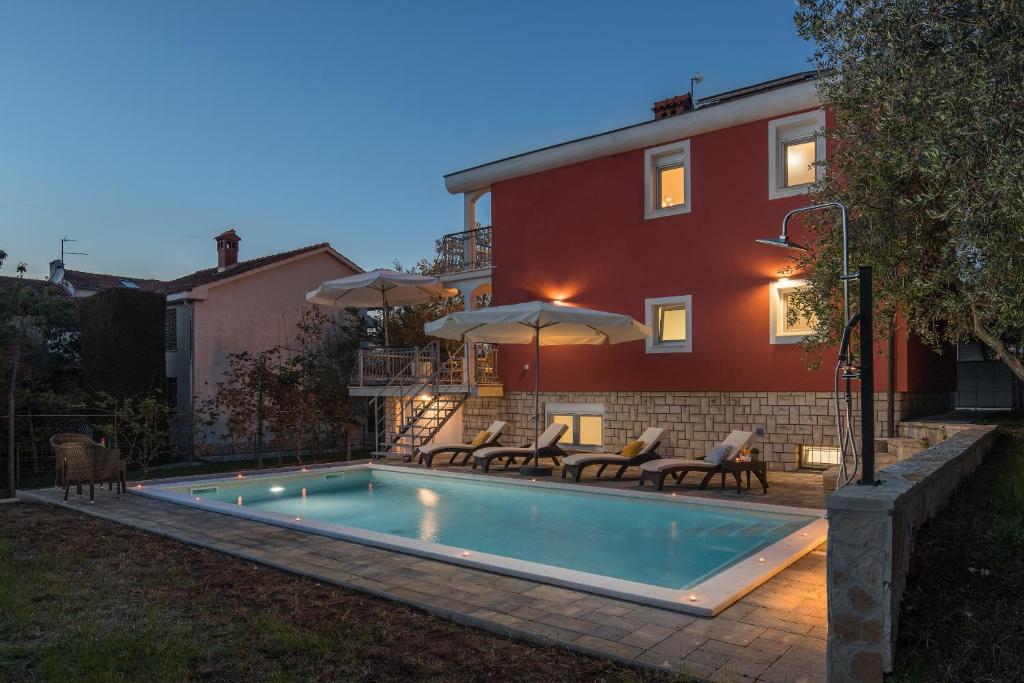una piscina con sedie e ombrelloni accanto a una casa di Villa Polion Peroj a Peroj