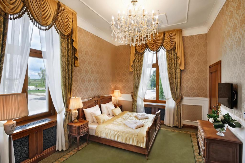a bedroom with a bed and a chandelier and windows at Pałac Mortęgi Hotel & SPA in Lubawa