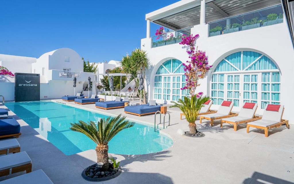 un complejo con piscina, sillas y palmeras en Aressana Spa Hotel & Suites - Small Luxury Hotels of the World, en Fira