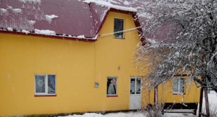 uma casa amarela com um telhado vermelho na neve em Біля комори em Pilipets