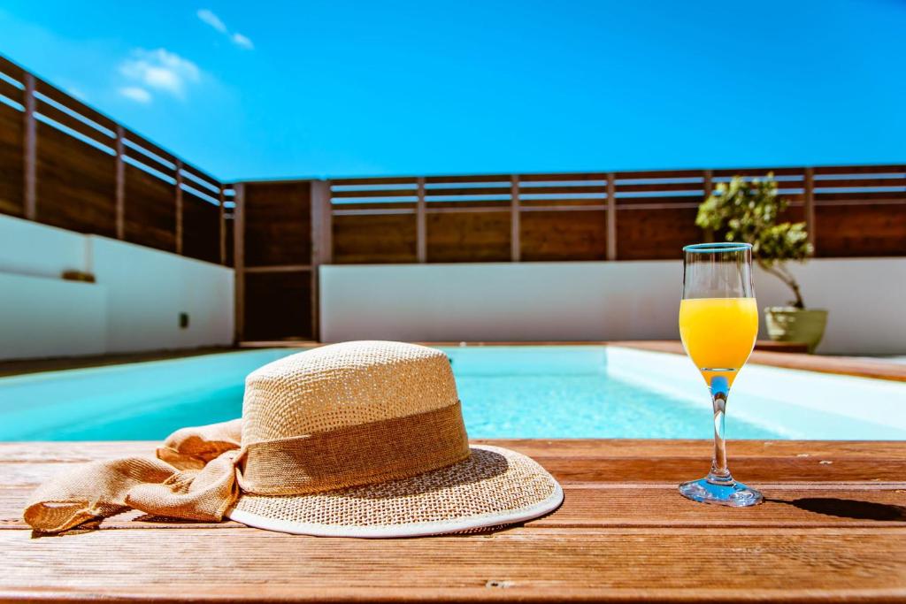 a straw hat and a glass of orange juice next to a swimming pool at Chania Paradise Retreat - Falasarna Villa Nostalgia in Plátanos