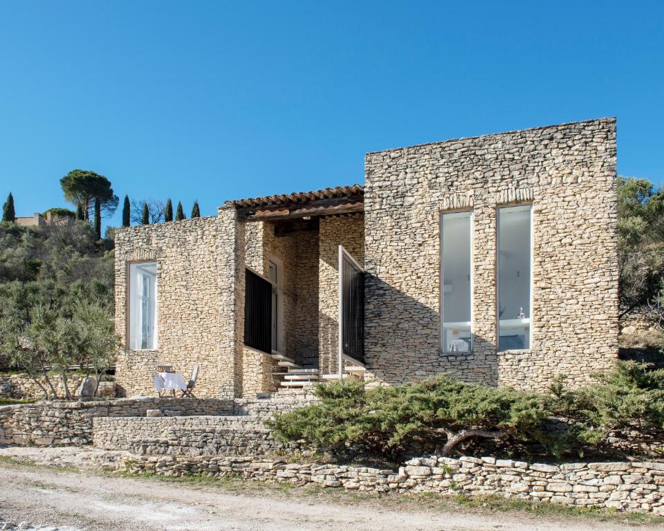 a brick house on a hill with a stone wall at Les Milles Roches in Gordes