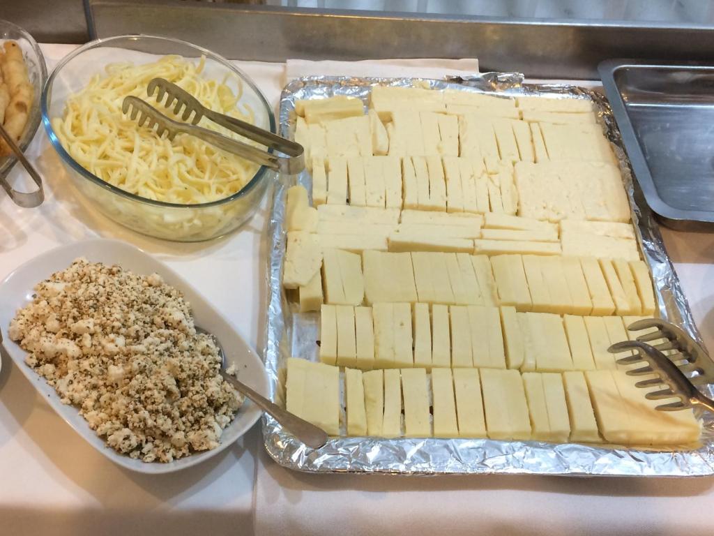 a table topped with cheese and a tray of pasta at Marigold Otel in Çeşme