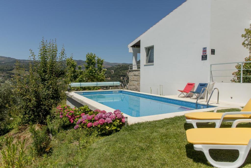 ein Haus mit einem Pool und einigen Stühlen und Blumen in der Unterkunft QUINTA DOS MONTEIROS - 3 Quartos com Piscina in Resende