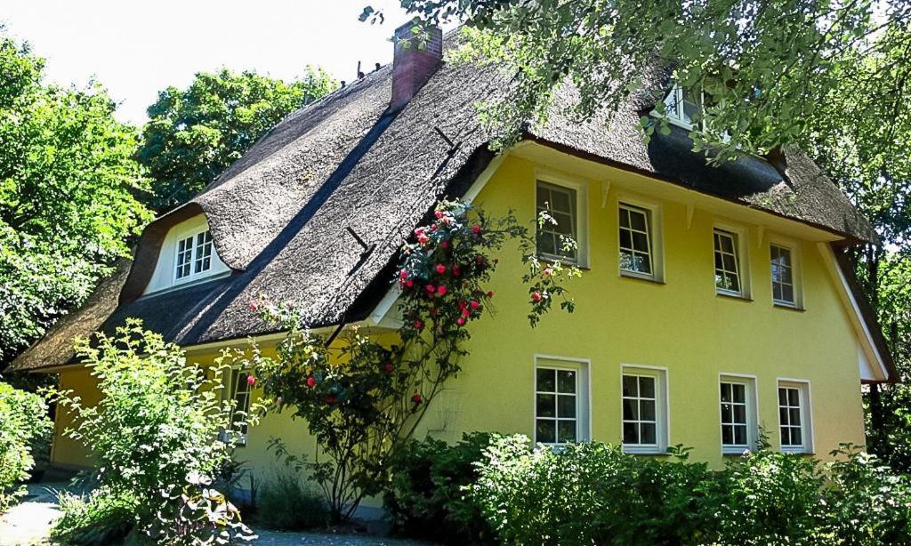 una casa amarilla con techo de paja y flores en Landhaus Butt 05, en Ahrenshoop