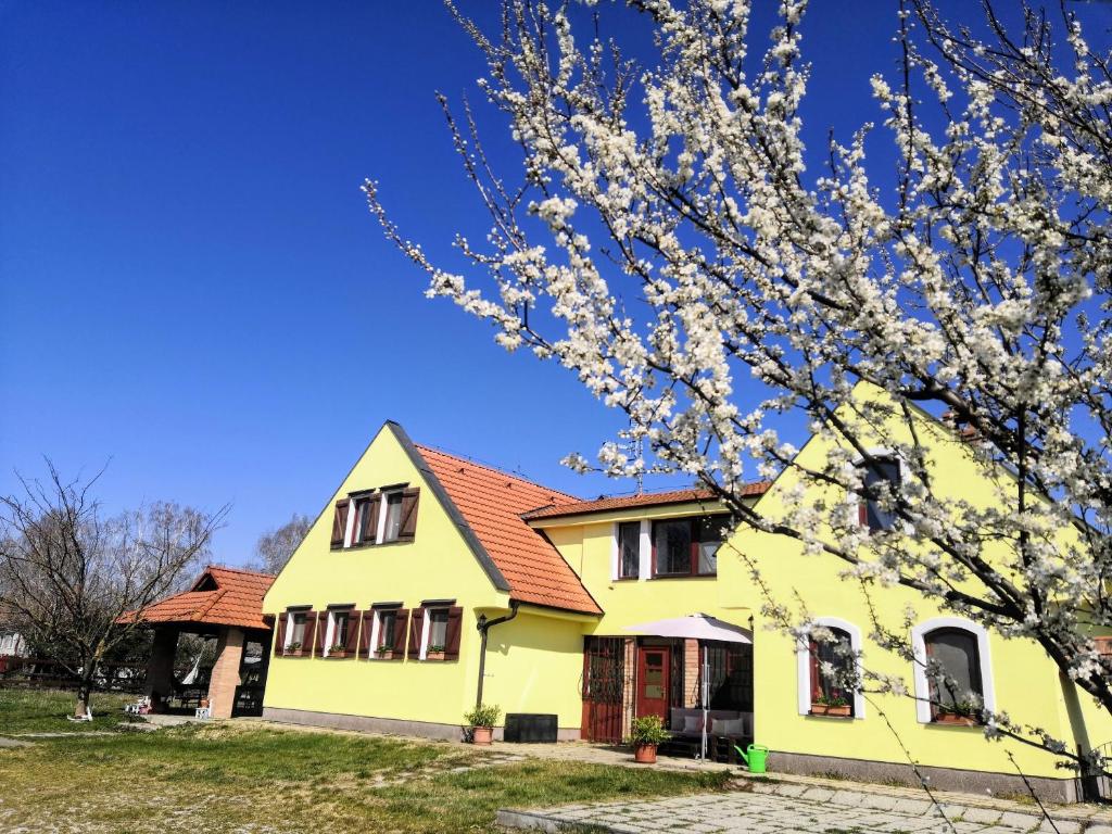 una casa amarilla con techo rojo y un árbol florido en Penzión Arkádia, en Kyselica