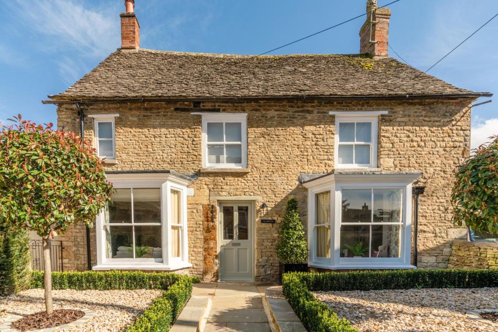 a stone house with white windows and bushes at Tachbrook in Charlbury