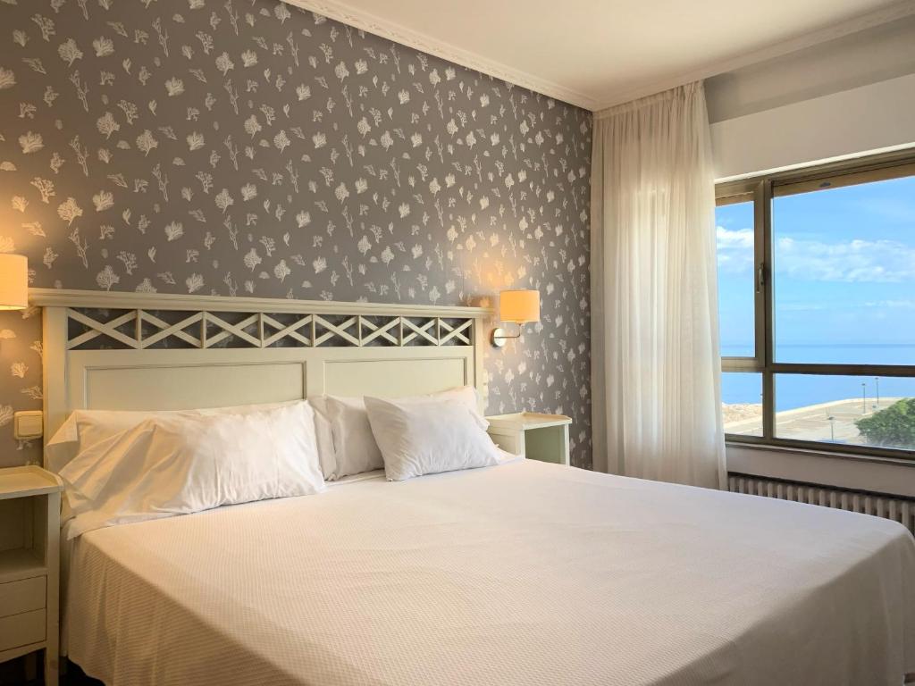 a bedroom with a white bed and a window at Hotel Playa de Los Locos in Suances