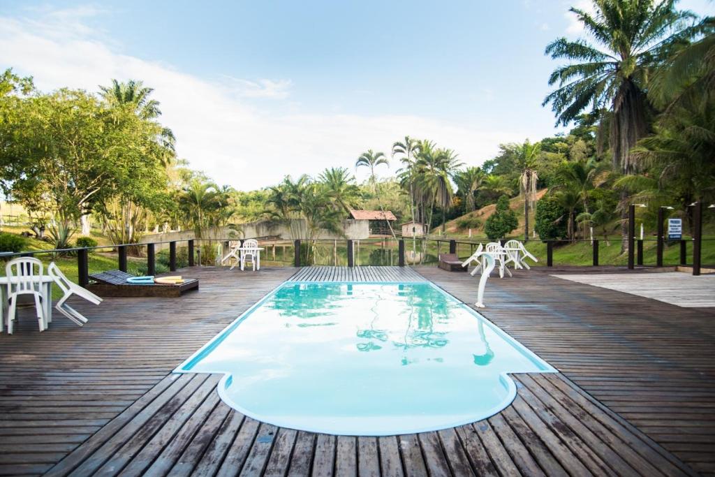 een zwembad op een houten terras met witte stoelen en tafels bij Hotel Fazenda VCP in Silva Jardim